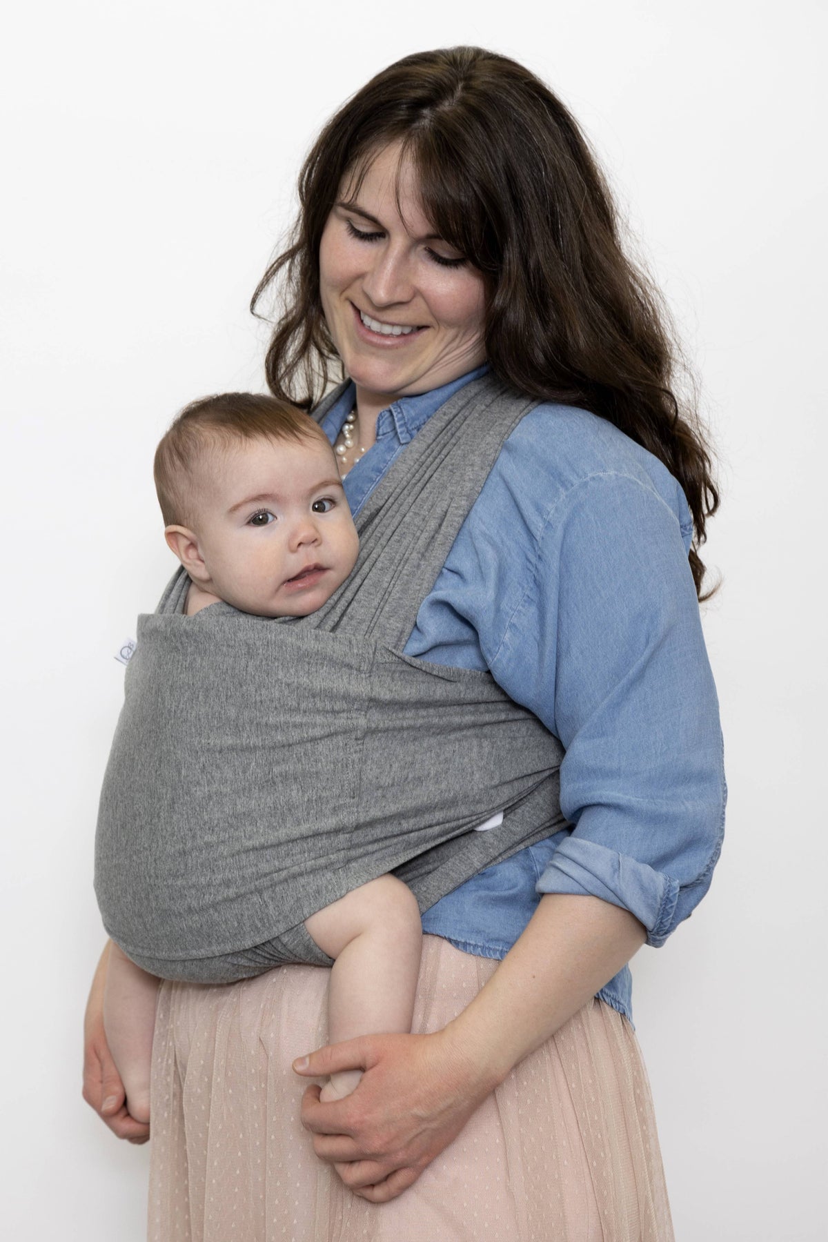 Woman holding a baby in a gray sling against a white background