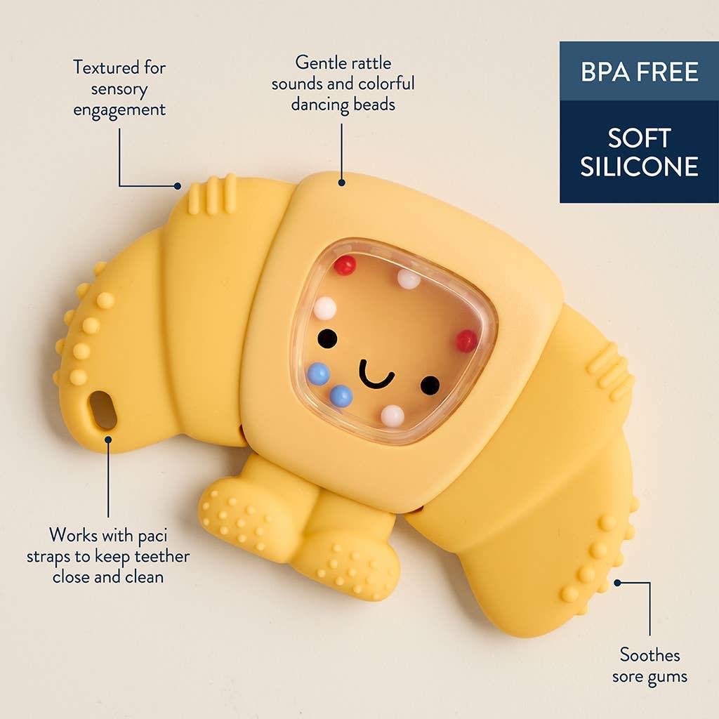 Yellow silicone croissant-shaped teether with text highlighting features on a beige background