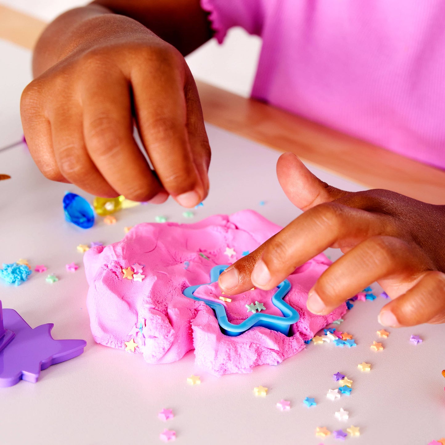 Children playing with pink play dough and cookie cutters on a white surface.